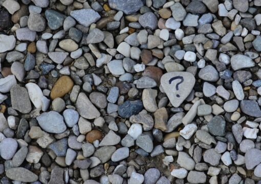 Pebbles on a beach. One pebble has a question mark draw on it.